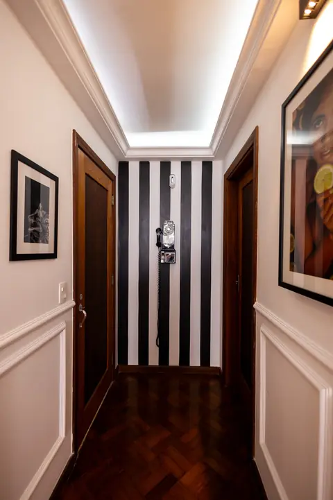 Corredor com quadros e parede listrada em preto e branco ao fundo