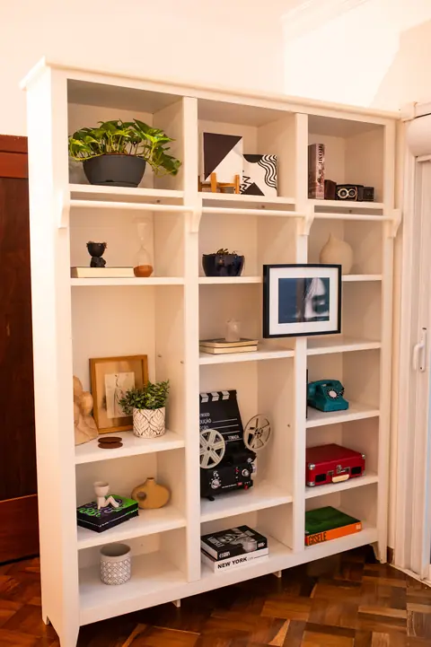 Estante branca com câmeras antigas, livros, plantas e quadros