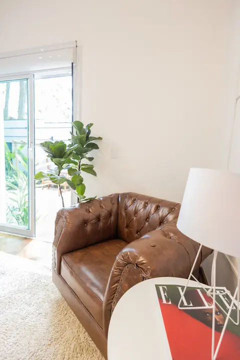 Poltrona chesterfield de couro ao lado da janela, com abajur e planta