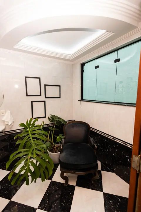 Banheiro com piso xadrez preto e branco, poltrona e molduras vazias