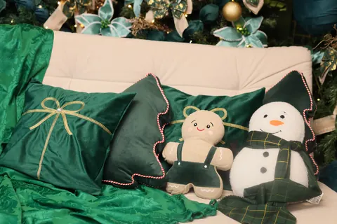 Almofadas de veludo verde, boneco de gengibre e boneco de neve de pelúcia sobre o sofá do cenário de Natal