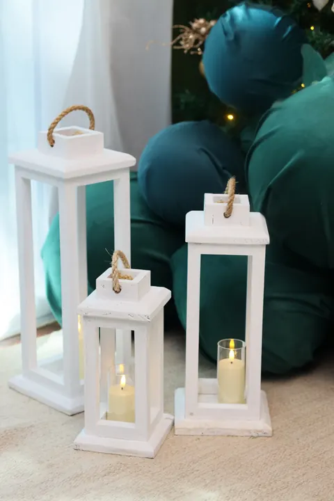 Lanternas brancas com velas de LED junto às bolas de veludo verde do cenário de Natal
