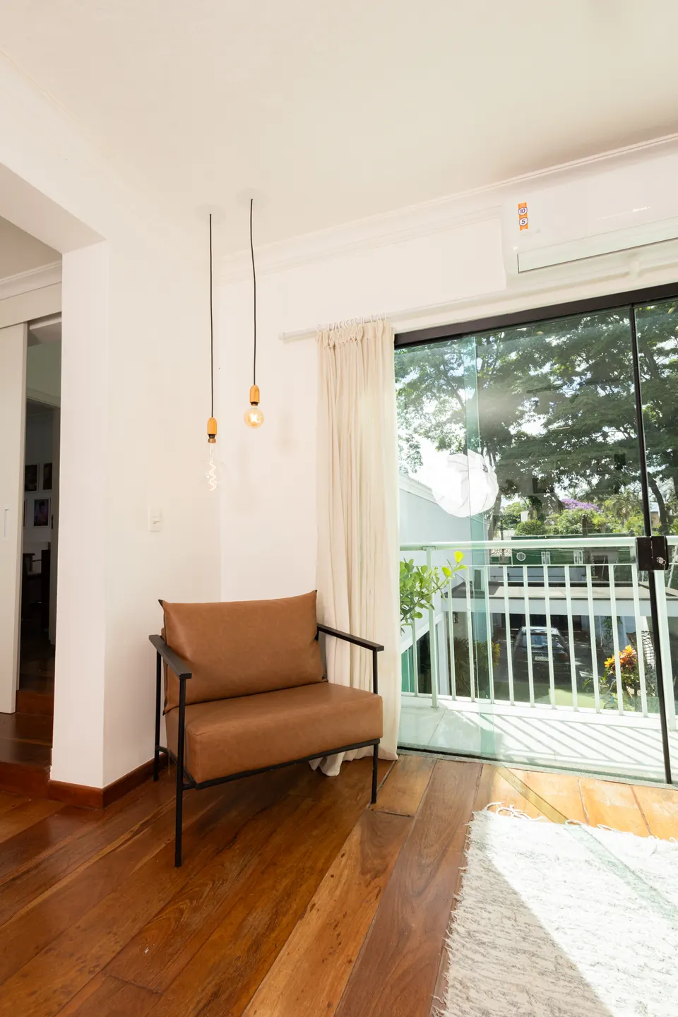 Poltrona de couro junto à porta de vidro com luz natural e vista para as árvores no Loft Lumière