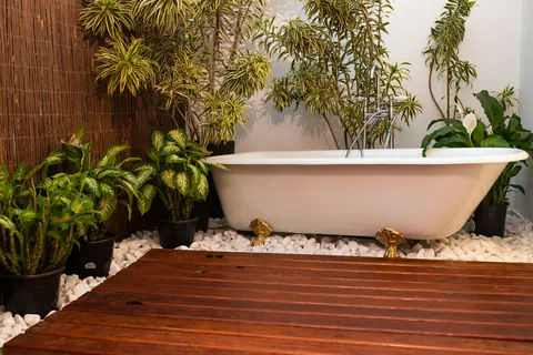 Banheira vitoriana com pés dourados entre plantas tropicais e pedras brancas no Estúdio Majestic