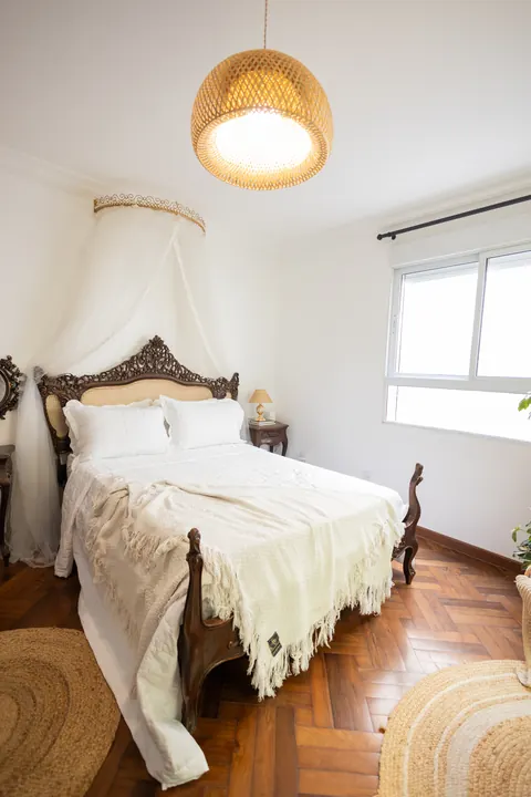 Quarto com luz natural, cama entalhada e luminária de palha no Estúdio Majestic
