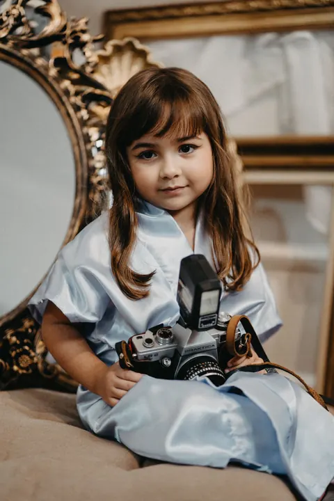 Daminha de roupão azul segurando uma câmera fotográfica antiga ao lado de espelho dourado