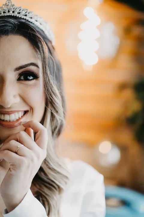 Retrato da noiva de tiara sorrindo, com luzes desfocadas ao fundo