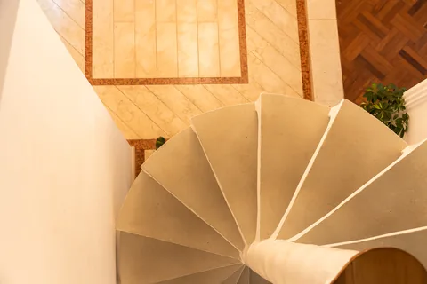 Degraus da escada escultural vistos de cima, sobre o piso de taco