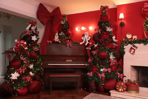 Piano, lareira e arandelas acesas no cenário de Natal vermelho do Loft Oásis