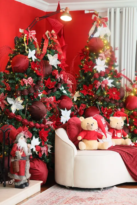Cenário de Natal vermelho do Loft Oásis com poltrona branca, ursinhos de pelúcia e árvores decoradas em vermelho e branco